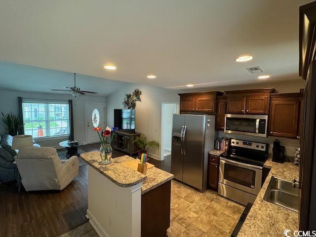 kitchen with appliances with stainless steel finishes, light stone counters, ceiling fan, sink, and a kitchen island