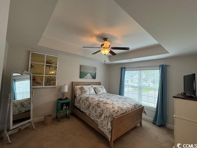 carpeted bedroom with ceiling fan and a tray ceiling