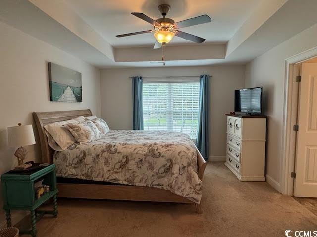 carpeted bedroom with a tray ceiling and ceiling fan