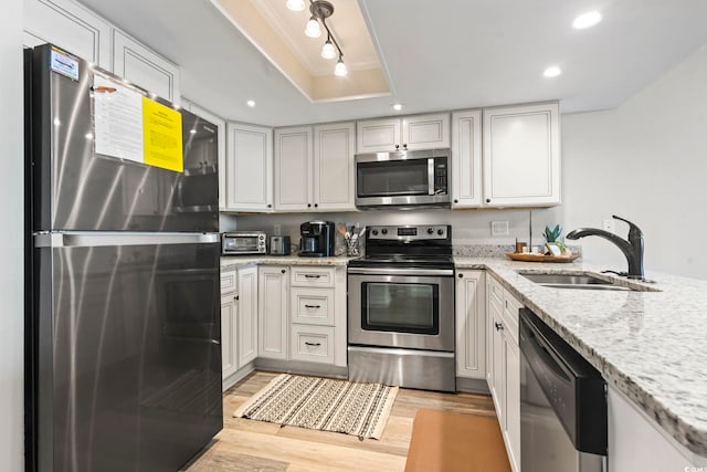 kitchen featuring light wood-type flooring, sink, white cabinetry, stainless steel appliances, and light stone countertops