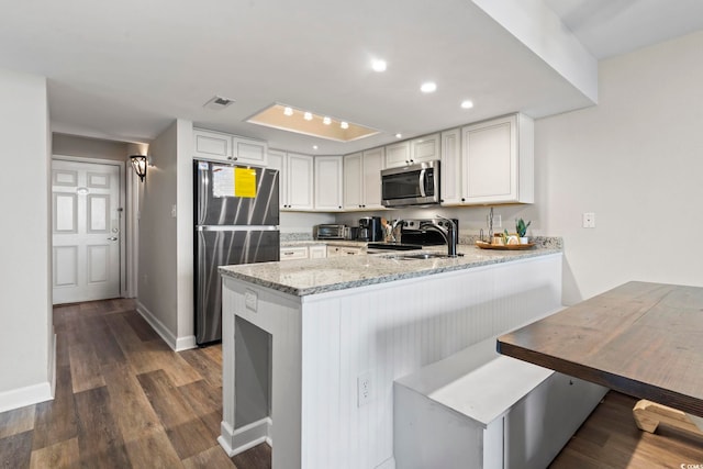 kitchen featuring light stone counters, kitchen peninsula, white cabinetry, appliances with stainless steel finishes, and dark hardwood / wood-style flooring