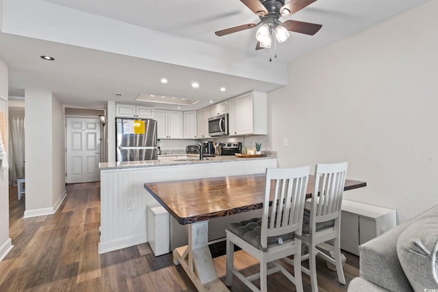 kitchen with white cabinetry, kitchen peninsula, appliances with stainless steel finishes, dark hardwood / wood-style flooring, and ceiling fan