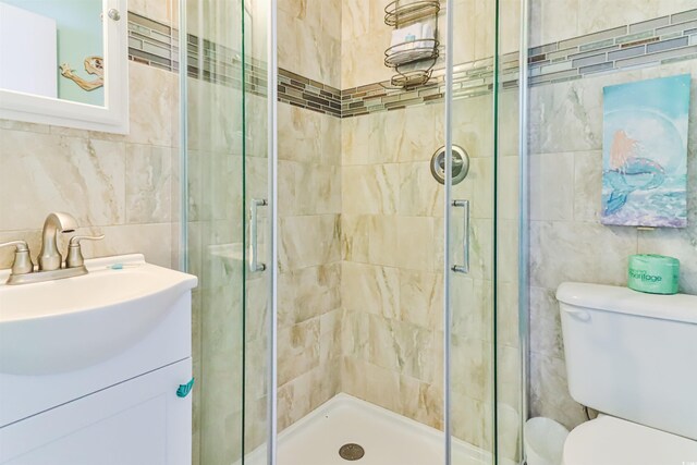 bathroom featuring a shower with door, vanity, toilet, and tile walls