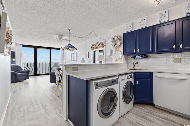 clothes washing area featuring sink, ceiling fan, washing machine and dryer, light wood-type flooring, and a textured ceiling