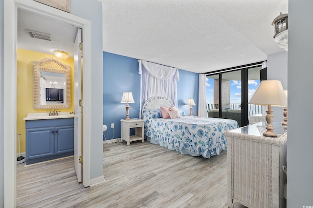 bedroom with access to exterior, sink, expansive windows, light hardwood / wood-style floors, and a textured ceiling