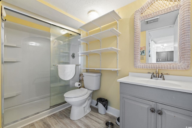 bathroom with vanity, a textured ceiling, a shower with door, hardwood / wood-style flooring, and toilet