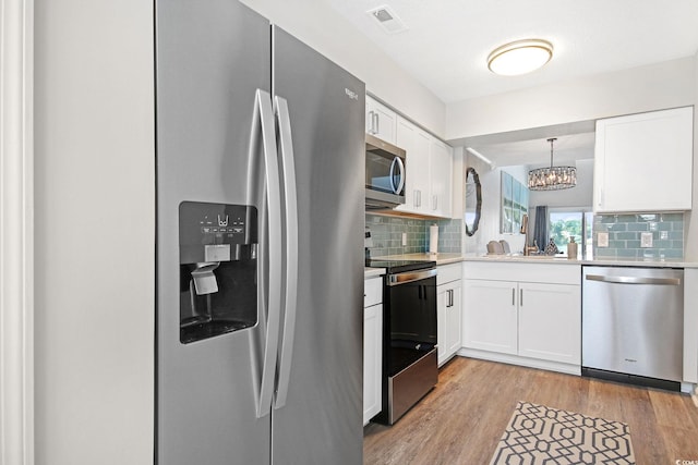 kitchen with appliances with stainless steel finishes, light wood-type flooring, pendant lighting, and white cabinets