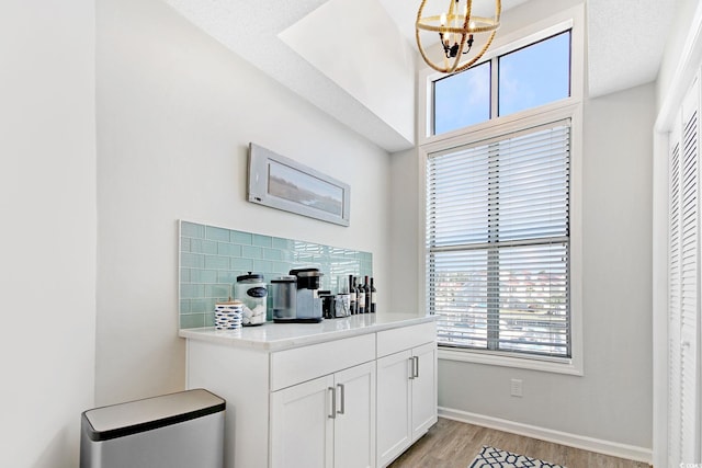 bar featuring tasteful backsplash, white cabinets, pendant lighting, a textured ceiling, and light hardwood / wood-style flooring