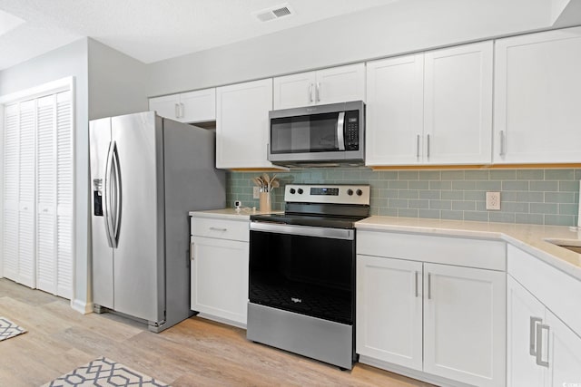 kitchen featuring stainless steel appliances, light wood-type flooring, tasteful backsplash, and white cabinetry