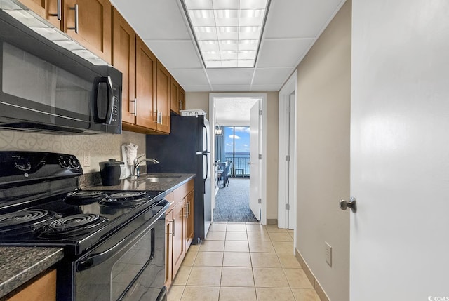 kitchen with electric range, sink, a drop ceiling, light tile patterned floors, and dark stone countertops