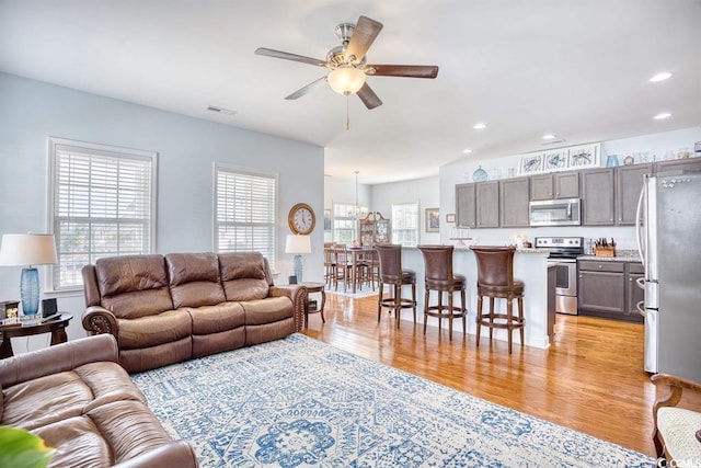 living room with ceiling fan with notable chandelier and light wood-type flooring