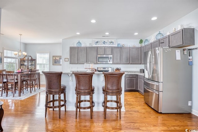 kitchen with light wood-type flooring, hanging light fixtures, an inviting chandelier, and stainless steel appliances