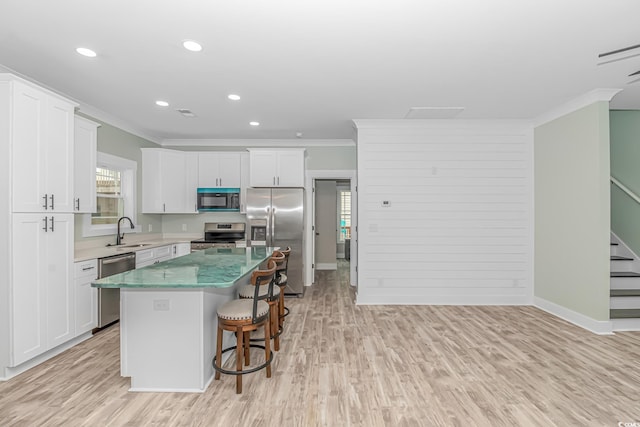 kitchen with sink, a kitchen island, light hardwood / wood-style flooring, appliances with stainless steel finishes, and crown molding