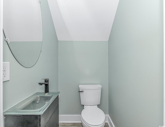 bathroom with toilet, hardwood / wood-style flooring, vaulted ceiling, and vanity