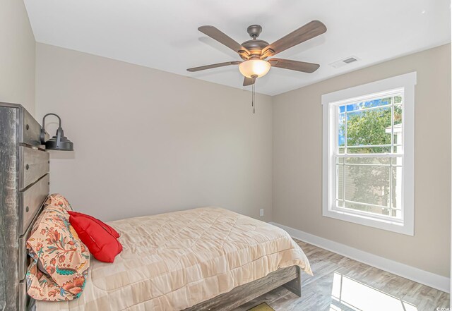 bedroom with baseboards, a ceiling fan, wood finished floors, and visible vents
