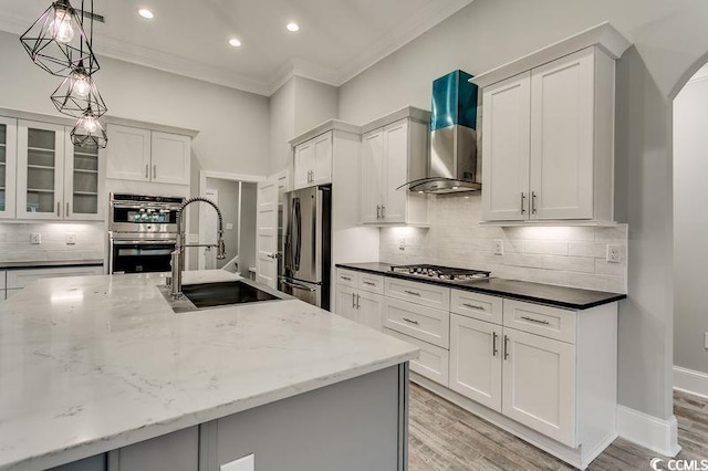 kitchen featuring ornamental molding, decorative light fixtures, wall chimney range hood, appliances with stainless steel finishes, and dark stone counters