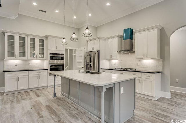 kitchen featuring pendant lighting, an island with sink, sink, wall chimney range hood, and stainless steel appliances