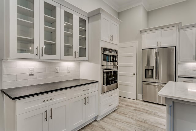 kitchen featuring light wood-type flooring, white cabinets, stainless steel appliances, backsplash, and ornamental molding