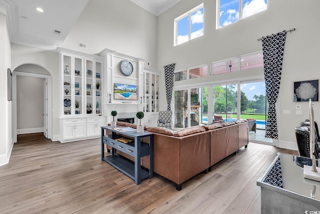 living room with ornamental molding, a towering ceiling, and light hardwood / wood-style floors