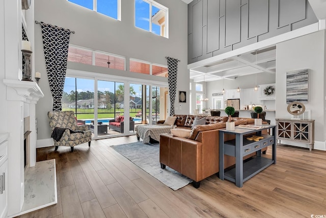 living room featuring coffered ceiling, a fireplace, a high ceiling, and light hardwood / wood-style flooring