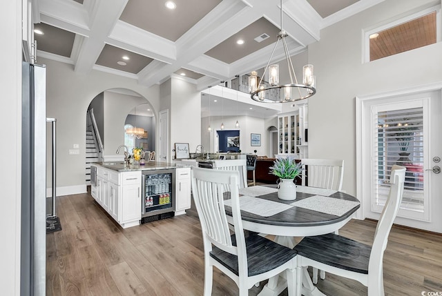 dining space featuring beamed ceiling, wine cooler, a chandelier, coffered ceiling, and light wood-type flooring