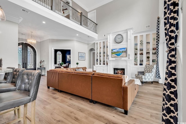 living room featuring light hardwood / wood-style flooring, crown molding, a chandelier, and a high ceiling