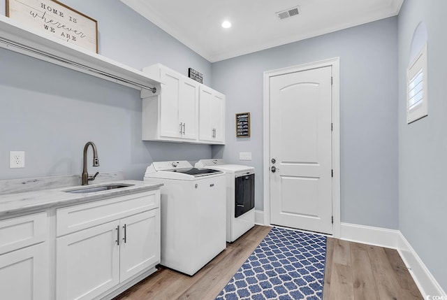 washroom featuring washer and dryer, sink, light hardwood / wood-style flooring, and cabinets