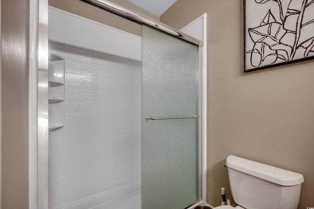 bathroom featuring a shower with door and toilet