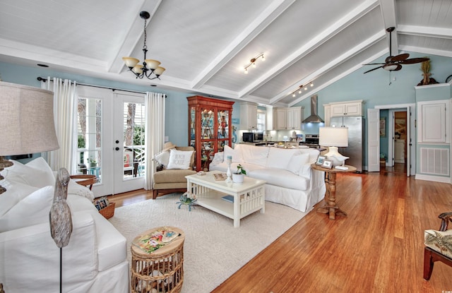 living room featuring vaulted ceiling with beams, ceiling fan with notable chandelier, french doors, and light wood-type flooring