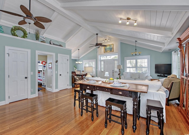 dining room featuring ceiling fan with notable chandelier, light hardwood / wood-style flooring, and vaulted ceiling with beams