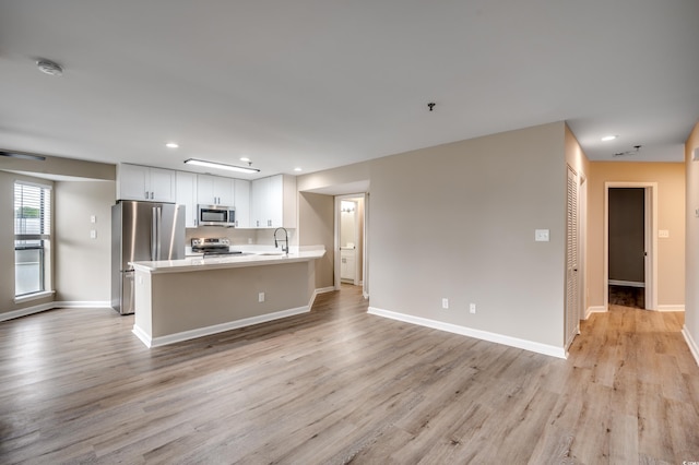 kitchen with appliances with stainless steel finishes, light hardwood / wood-style floors, white cabinetry, and sink