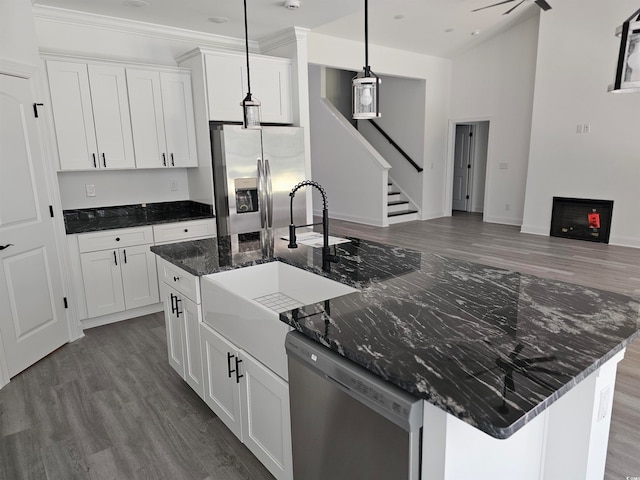 kitchen featuring pendant lighting, dark stone counters, an island with sink, white cabinets, and stainless steel appliances