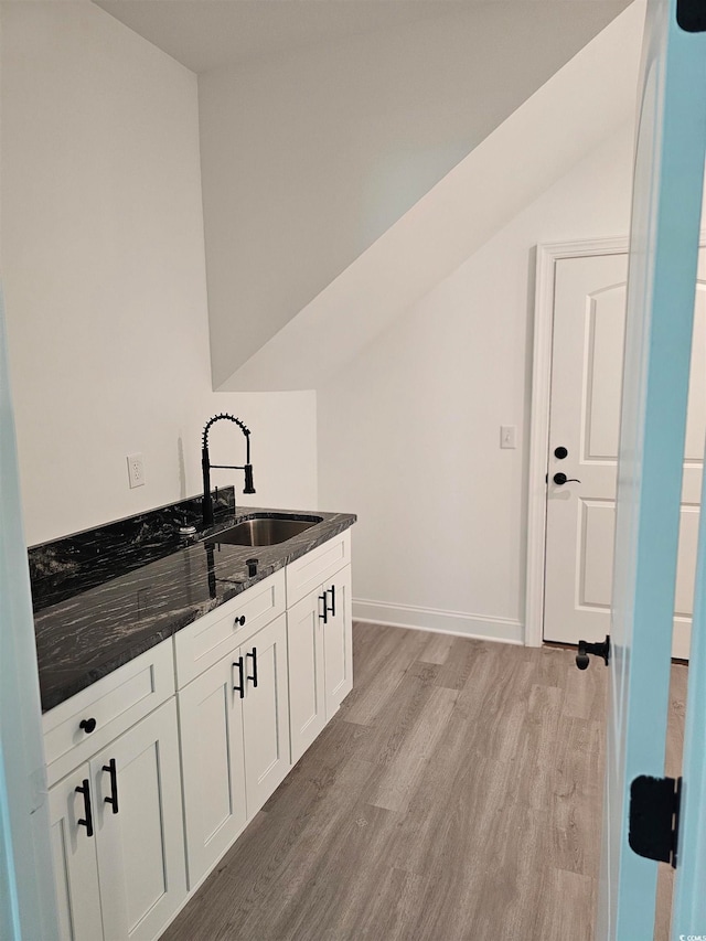 kitchen featuring light wood-type flooring, dark stone counters, white cabinetry, and sink