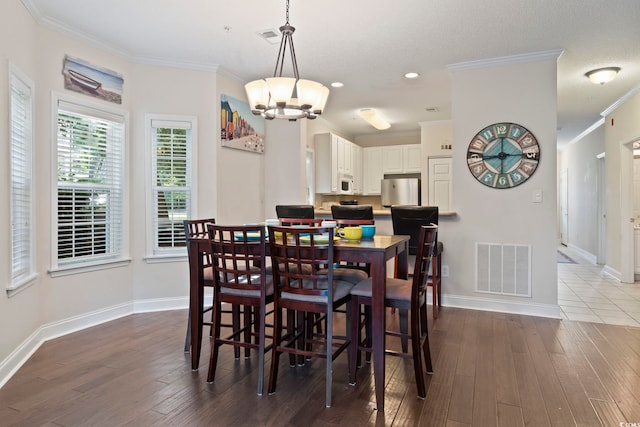 dining area featuring an inviting chandelier, wood-type flooring, a textured ceiling, and ornamental molding