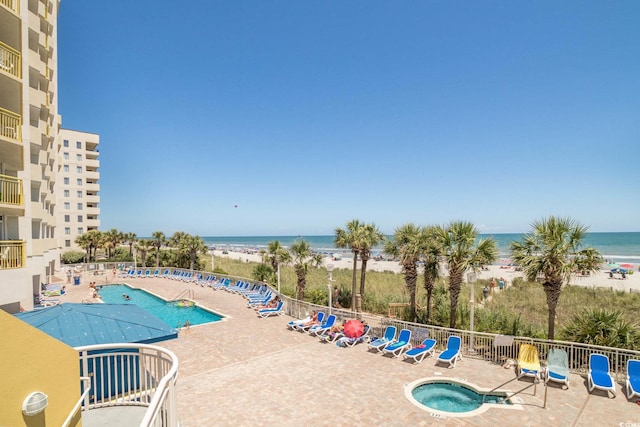 view of pool with a patio, a community hot tub, a water view, and a view of the beach