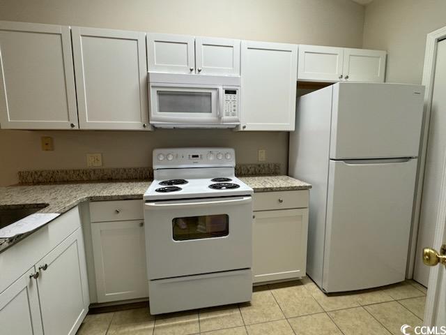 kitchen with white appliances, light tile patterned floors, and white cabinets