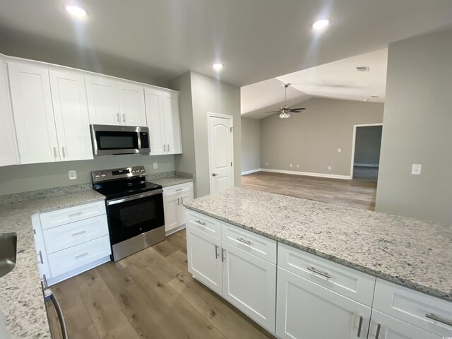 kitchen featuring light wood finished floors, ceiling fan, light stone countertops, stainless steel appliances, and white cabinetry
