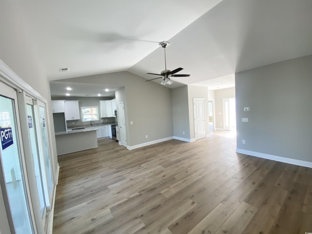 unfurnished living room with baseboards, lofted ceiling, a ceiling fan, and light wood finished floors