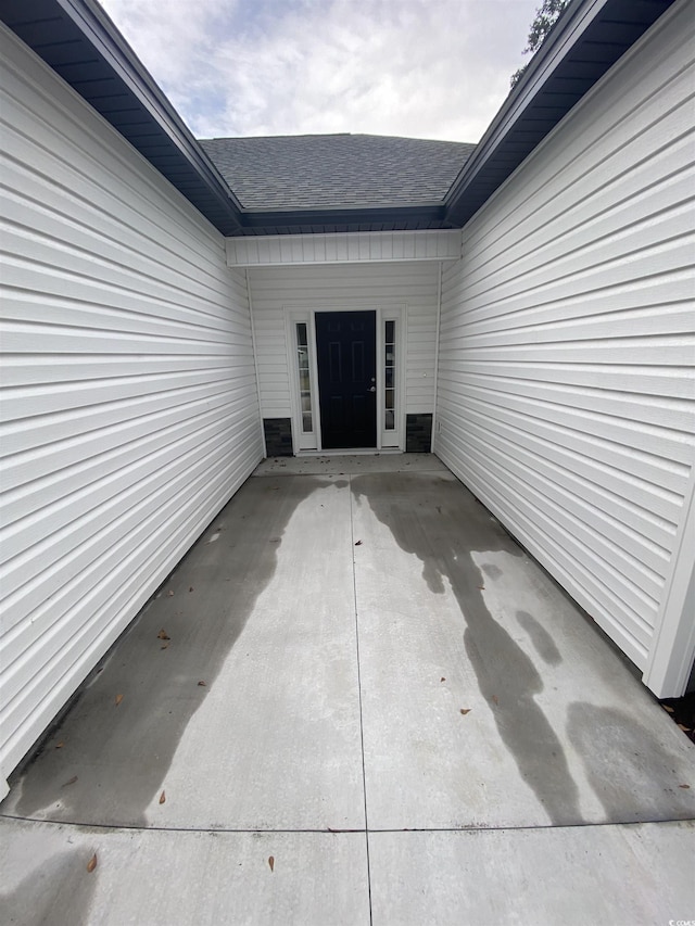 doorway to property featuring a patio and a shingled roof