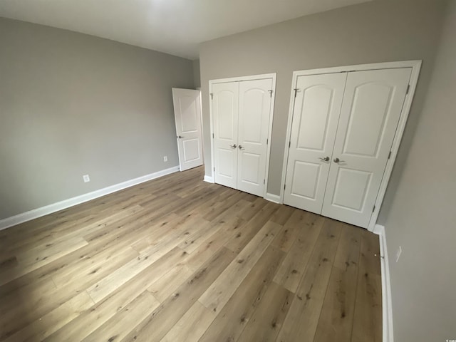 unfurnished bedroom featuring hardwood / wood-style floors, baseboards, and two closets
