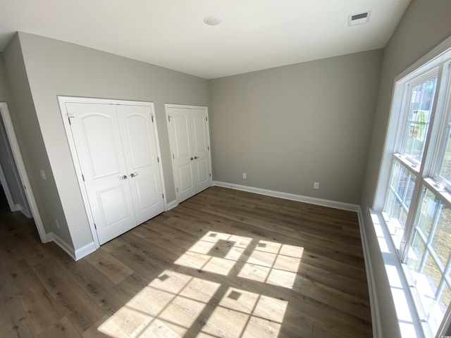 unfurnished bedroom with visible vents, multiple closets, baseboards, and wood finished floors