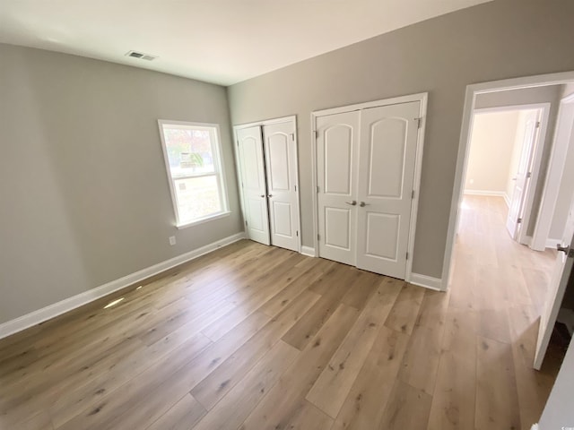 unfurnished bedroom featuring visible vents, baseboards, light wood-type flooring, and multiple closets