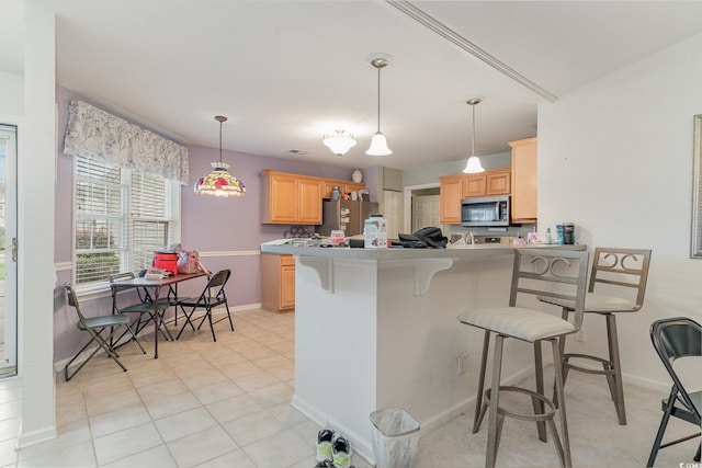 kitchen featuring light brown cabinetry, a breakfast bar area, light tile patterned floors, appliances with stainless steel finishes, and kitchen peninsula