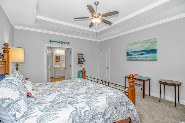 bedroom with a tray ceiling, light colored carpet, ensuite bath, ornamental molding, and ceiling fan