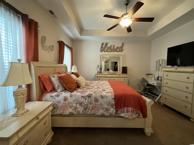 bedroom with multiple windows, visible vents, a raised ceiling, and dark colored carpet