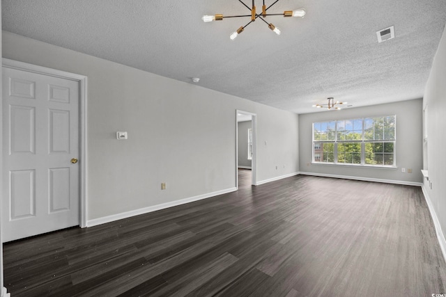 spare room featuring a chandelier, dark wood-type flooring, and a textured ceiling