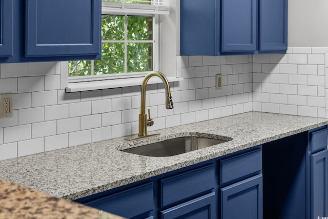 kitchen with blue cabinetry, light stone countertops, sink, and decorative backsplash