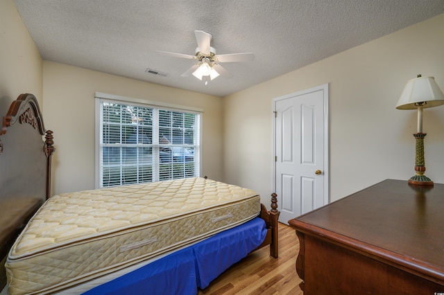 bedroom with light hardwood / wood-style floors, ceiling fan, and a textured ceiling