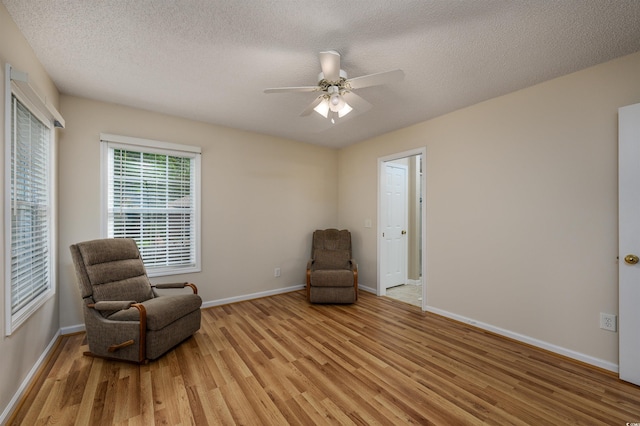 living area with a textured ceiling, ceiling fan, and light hardwood / wood-style flooring