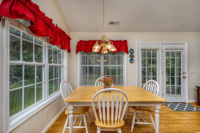 dining area featuring a notable chandelier, wood-type flooring, vaulted ceiling, and a textured ceiling